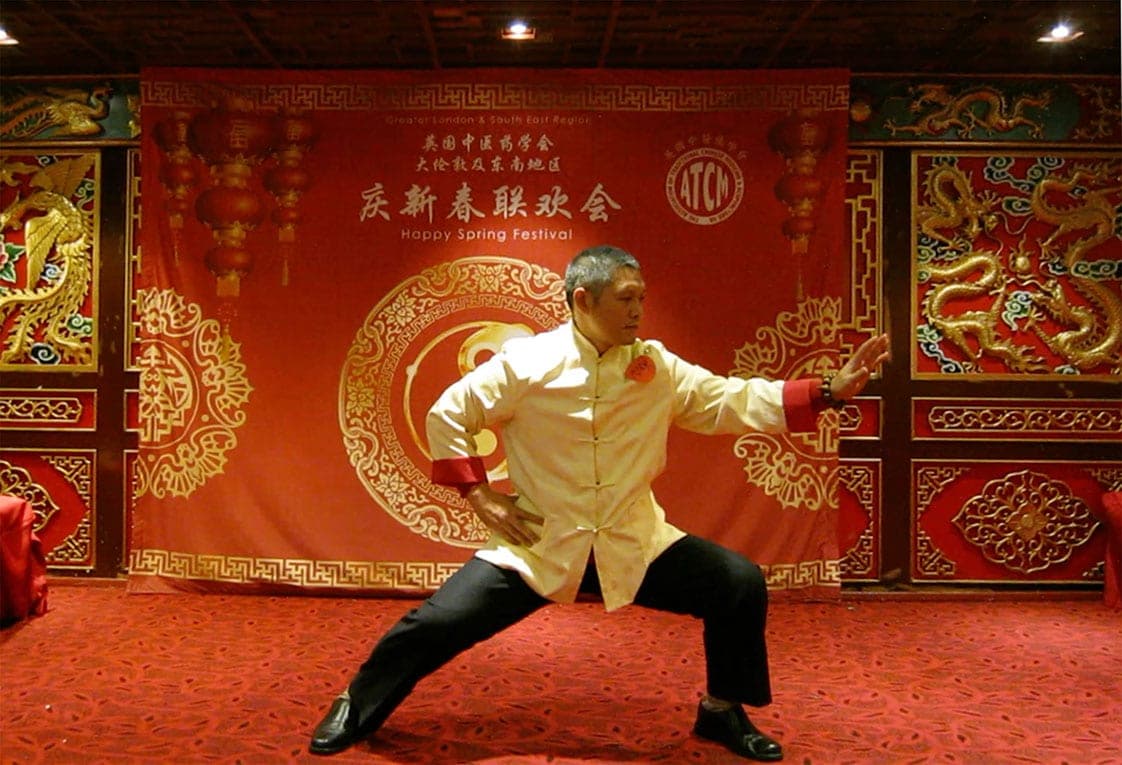 Shifu Liu in a low stance in front of a red ATCM Spring Festival backdrop