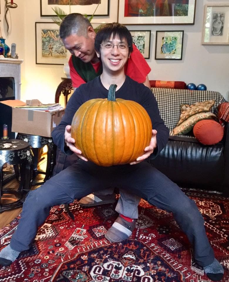 Shifu Liu checks the horse stance of a smiling student who holds a large pumpkin