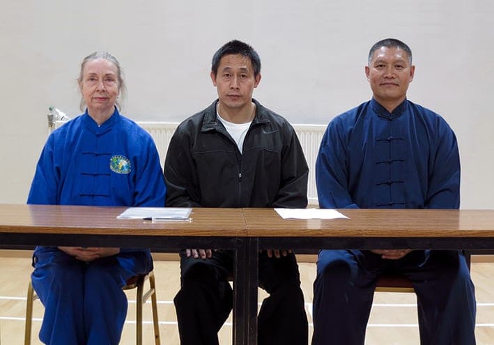Chris Jones, Master Chen Ziqiang and Shifu Liu seated side by side behind a table with papers on it