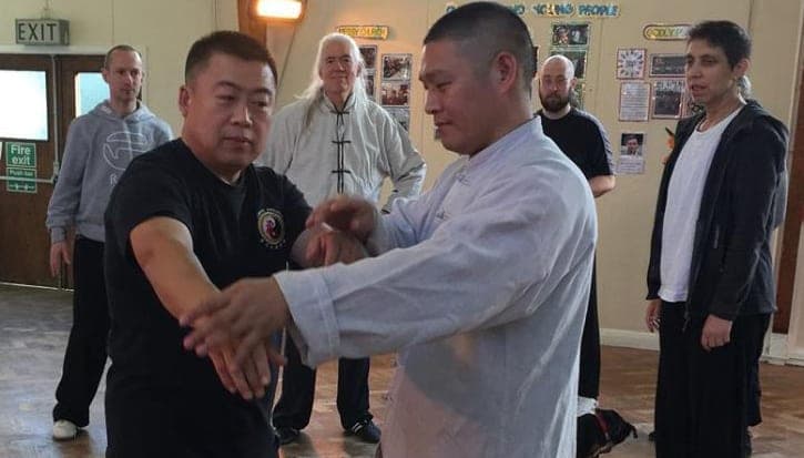 Grandmaster Zhu Changhai and Shifu Liu practise push hands in a church hall while students look on