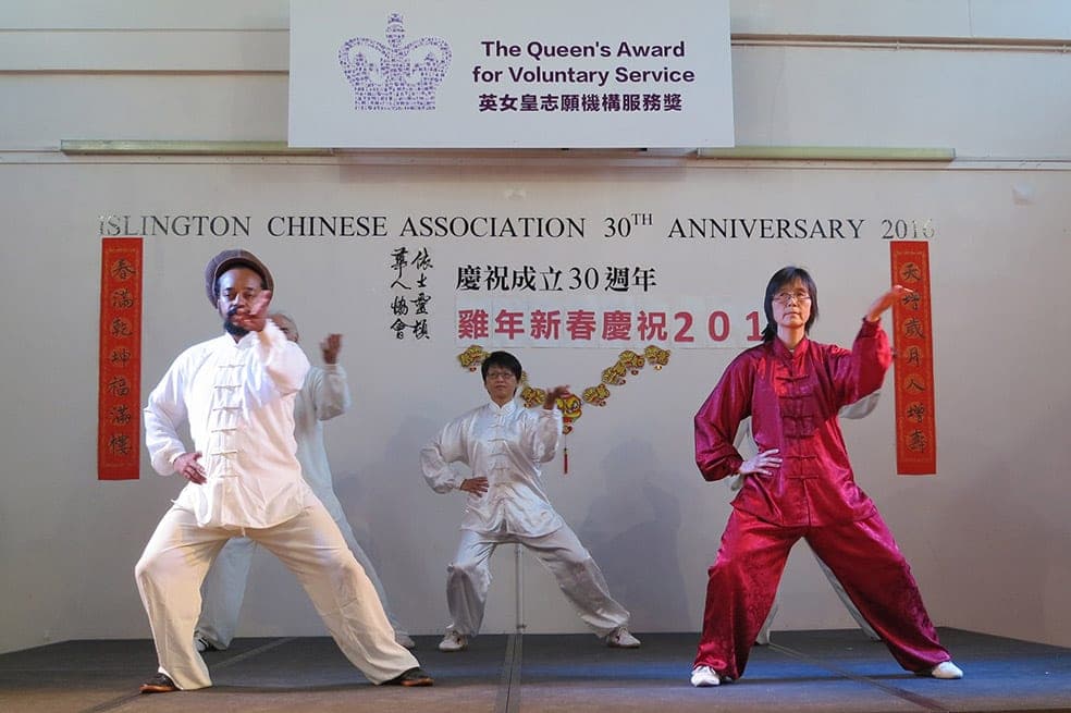 Students in silk uniforms perform Silk Reeling on a stage beneath an Islington Chinese Association anniversary banner