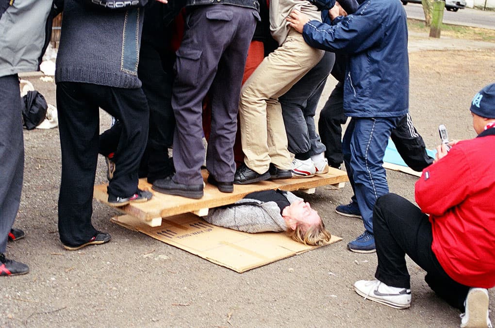 Student lying beneath a plank with several people standing on it during Ying Qi Gong testing