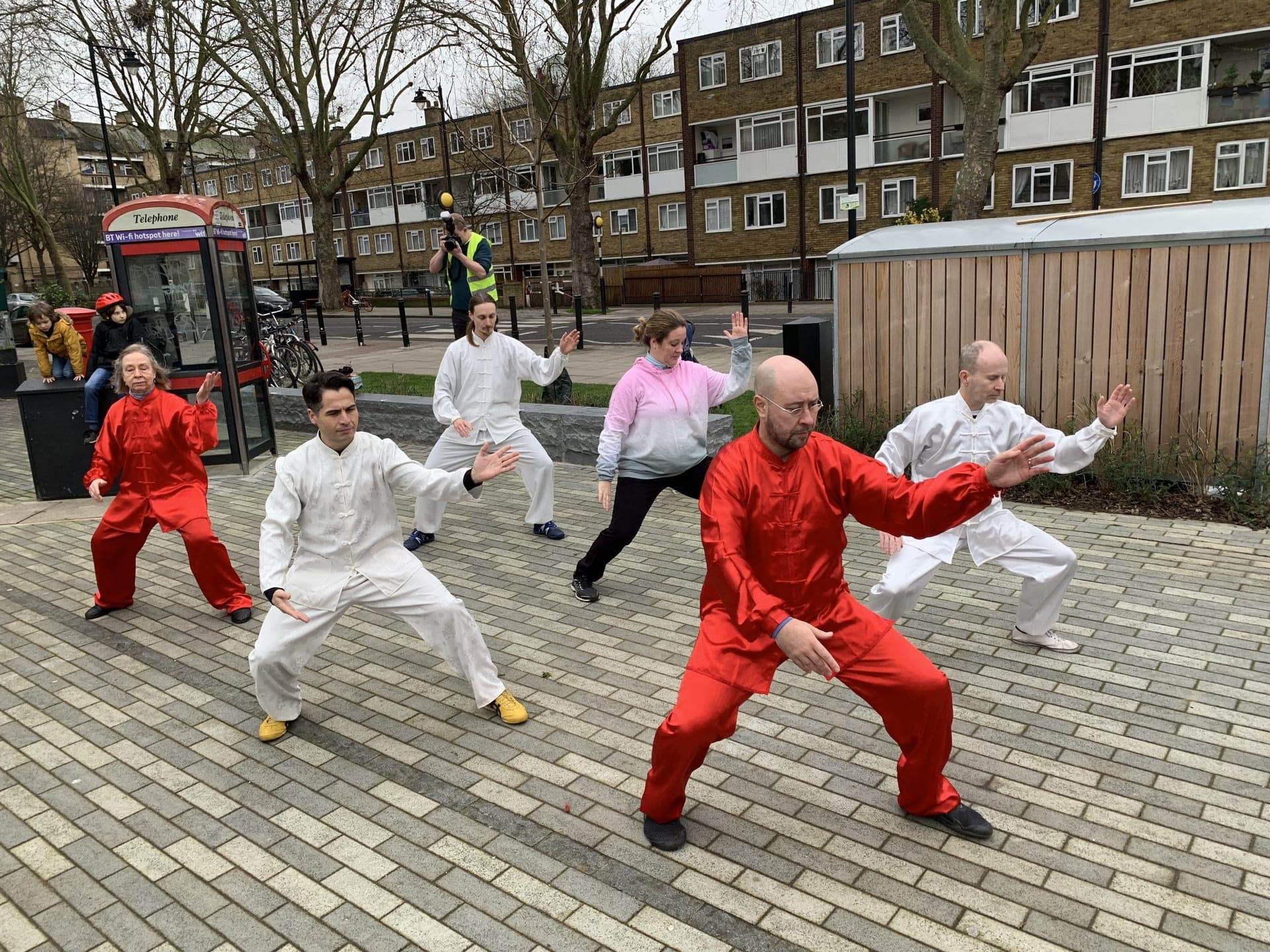 Students in red and white silk practising the 19 Form on the paved square beside a red telephone box