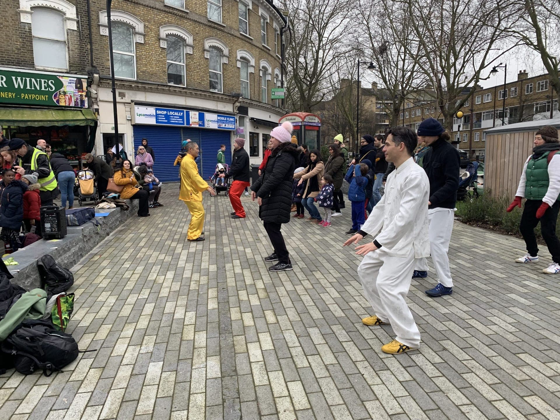 Members of the public in winter coats joining a Taiji practice led by performers in white and yellow
