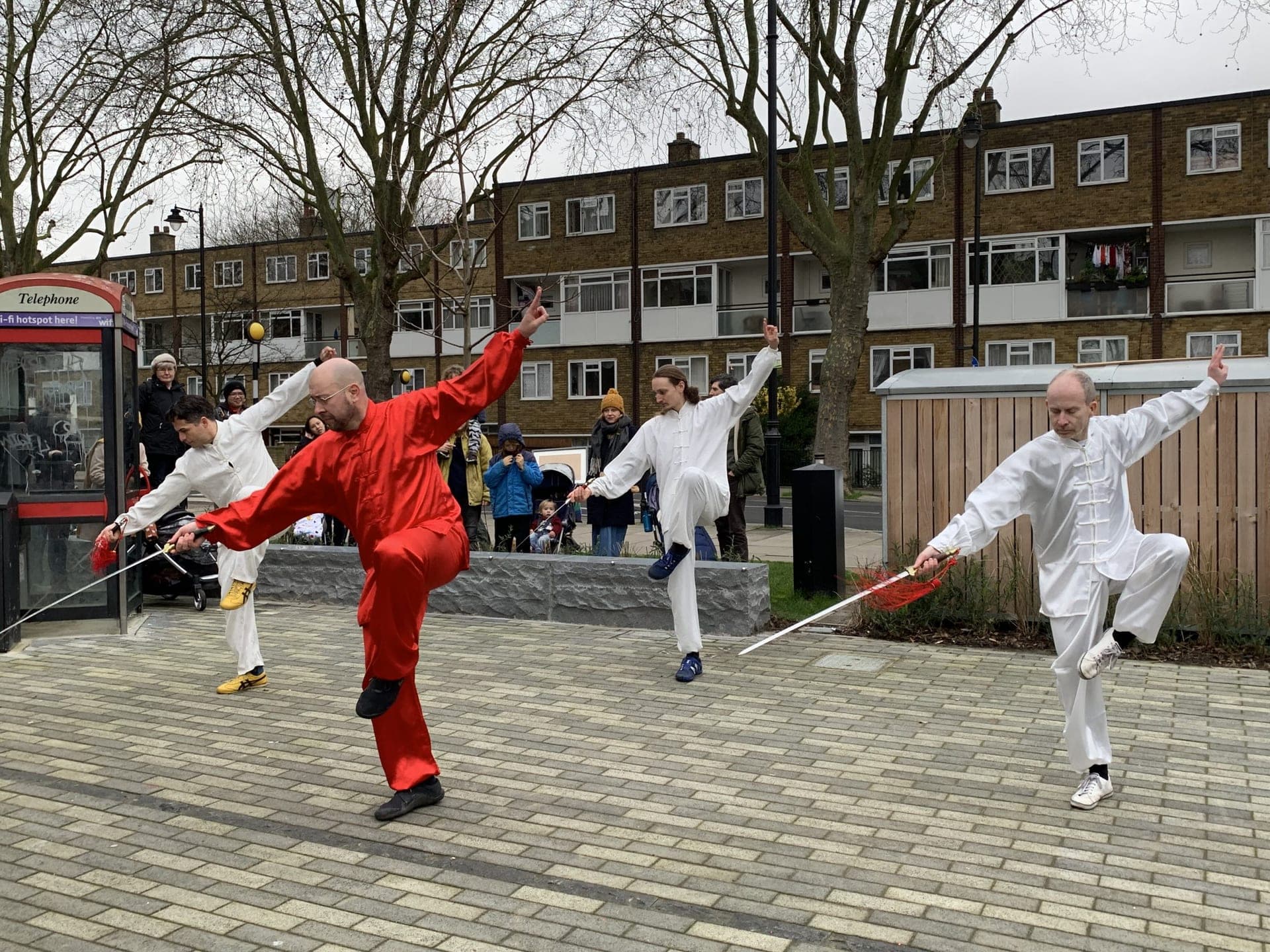 Performers in red and white balancing on one leg with straight swords during the sword form