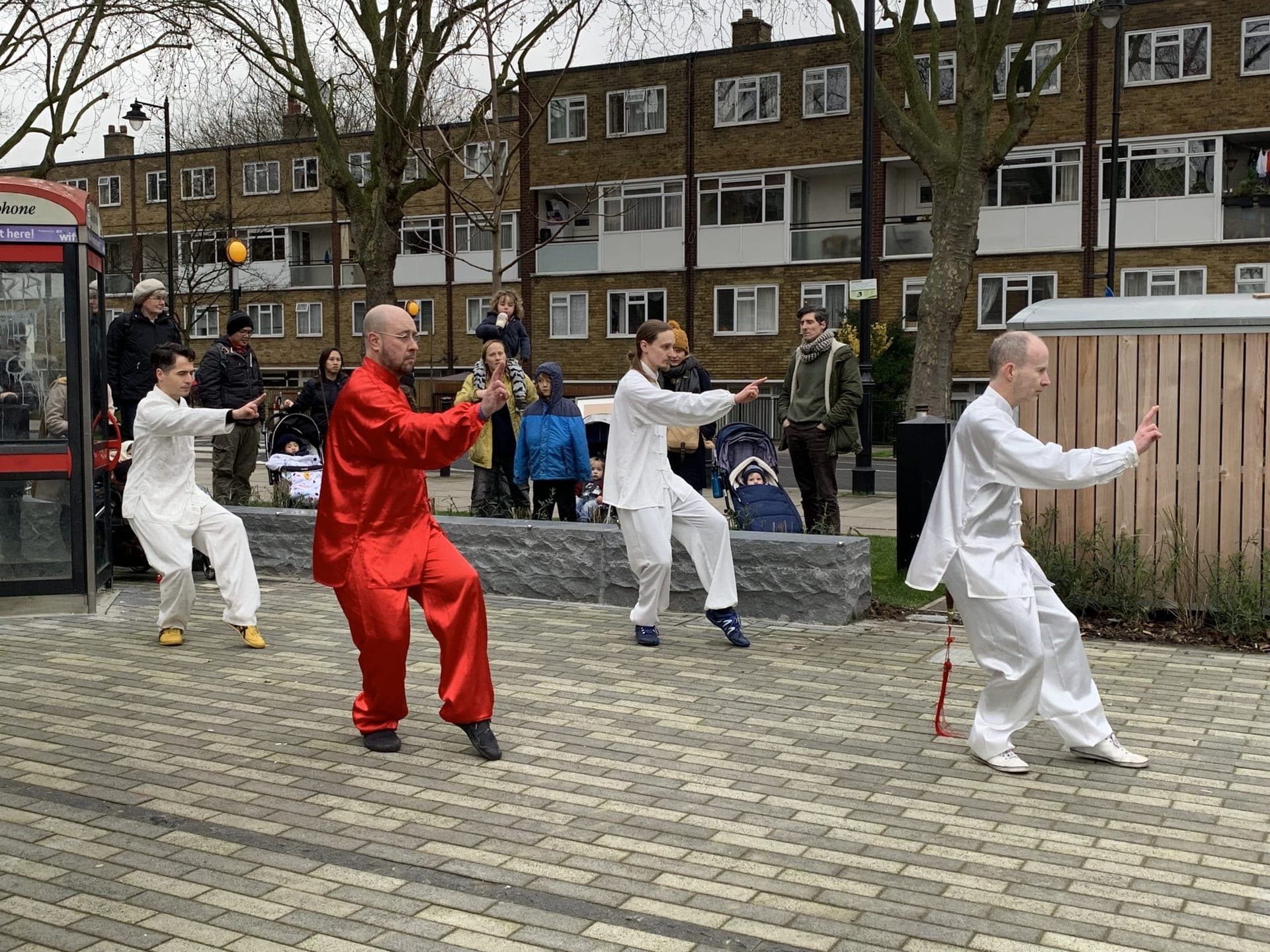 Four performers, one in red and three in white, spread across the square in Taiji postures