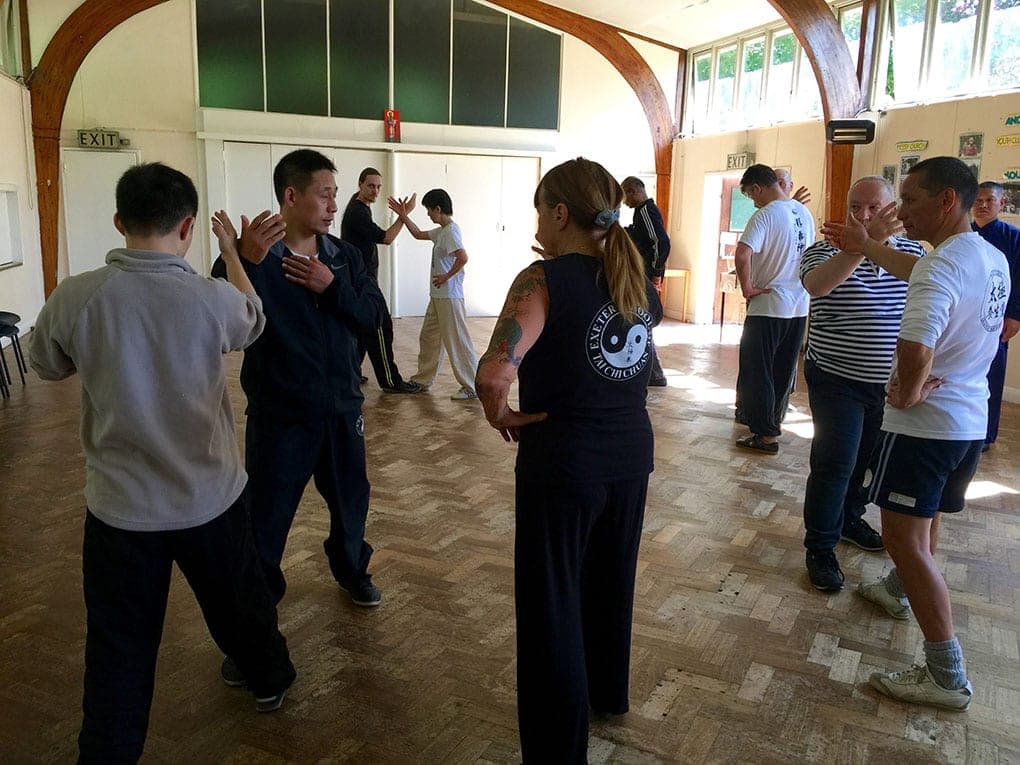 Pairs of students facing each other with hands raised, practising push hands across the hall