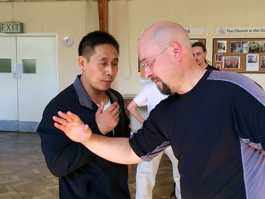 Close-up of two men in single-palm push hands, one with glasses and a beard
