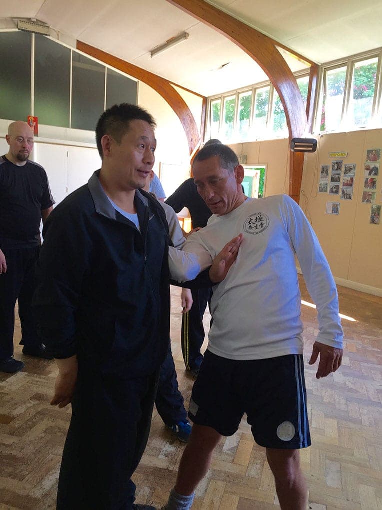 A teacher explains a push hands point to a smiling student in a white long-sleeved top