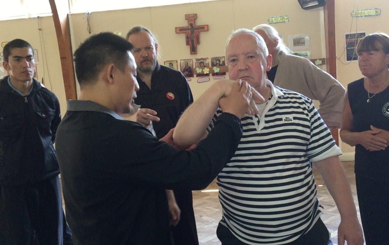 A teacher demonstrates a martial application, holding a student's wrist and elbow as a small group watches