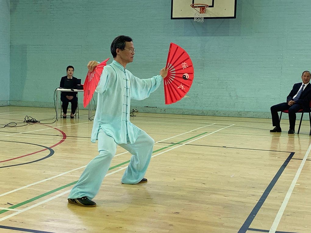 Yue Liming in pale blue silk performing the double fan form with two red fans