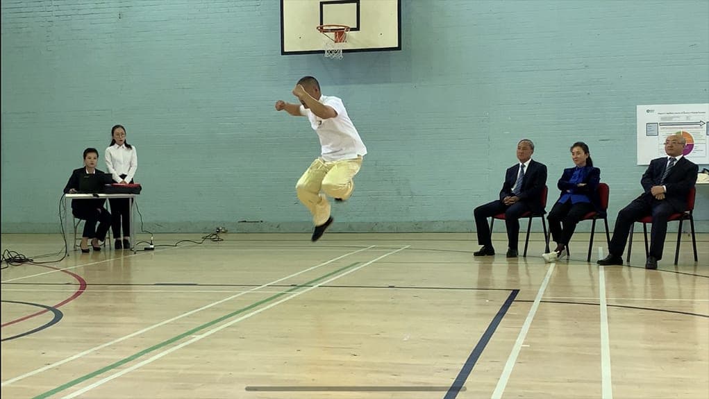 Shifu Liu airborne in a jump from Xinjia Erlu in the Edinburgh sports hall as seated guests watch