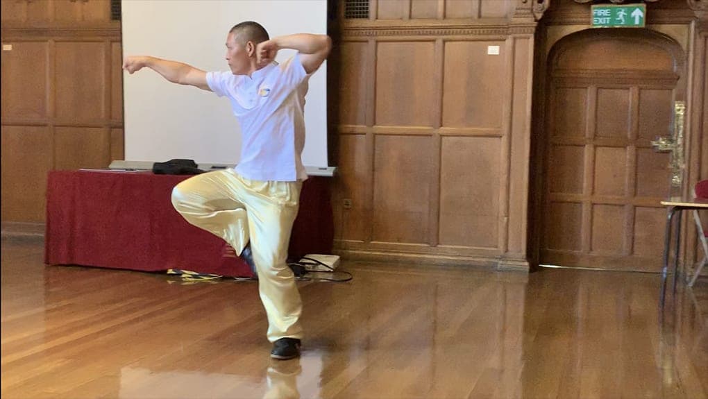 Shifu Liu balancing on one leg in a Xinjia posture in Oxford Town Hall