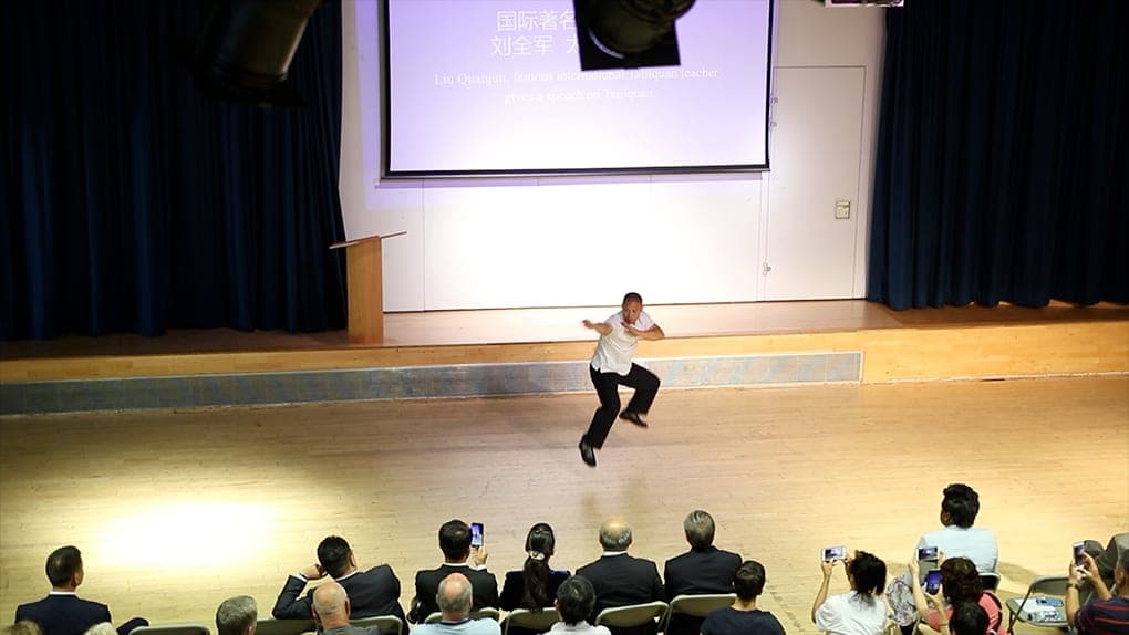 Shifu Liu in mid-air on the stage of the Haverstock School hall in front of the London audience