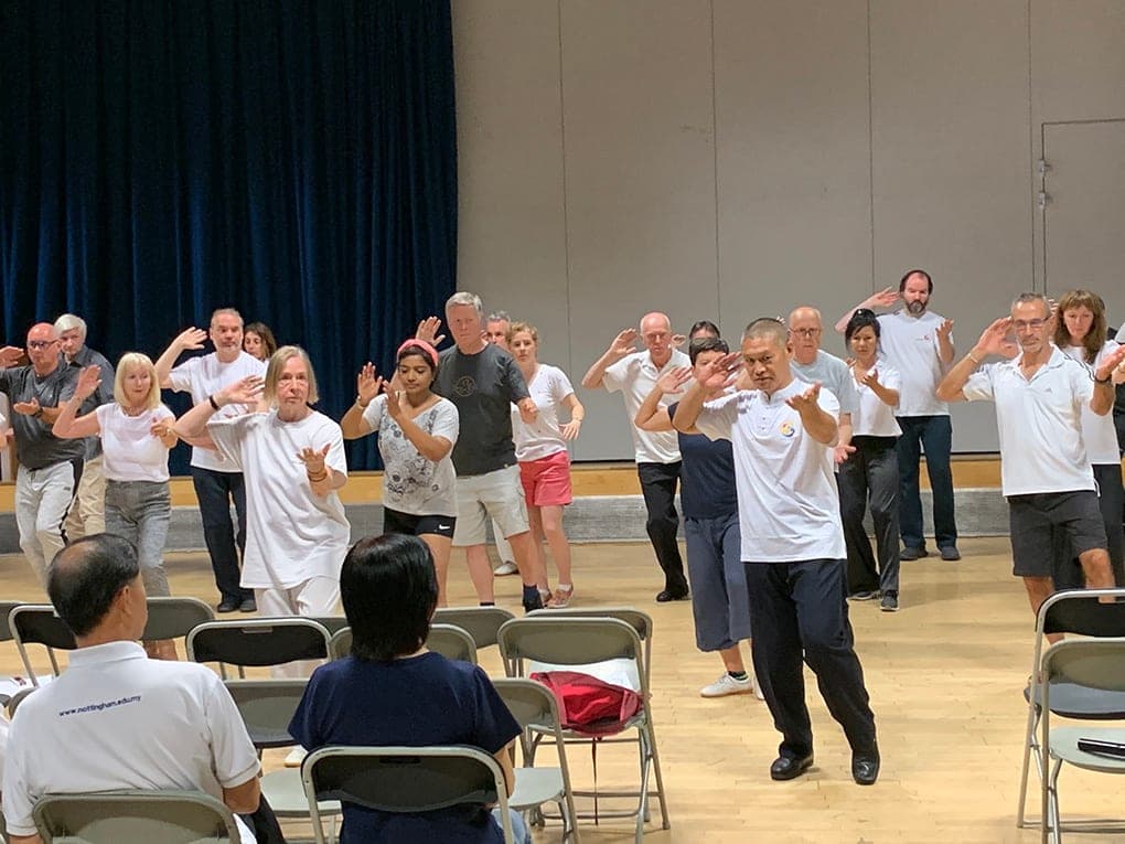 Shifu Liu leading the audience through Taiji stepping among rows of chairs in the London hall