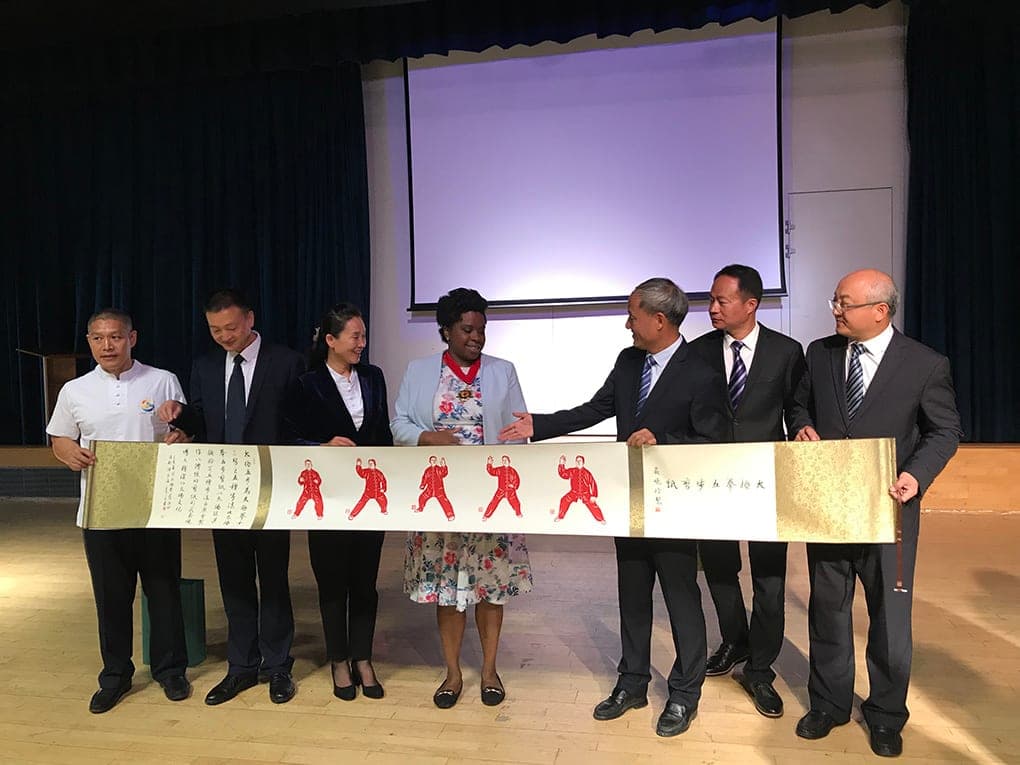 Members of the delegation and Councillor Sabrina Francis holding up a long painted scroll of Taiji figures