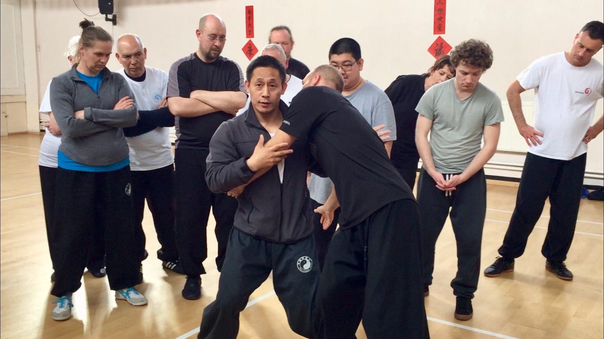 A teacher demonstrates a push hands application on a student while a circle of students watches