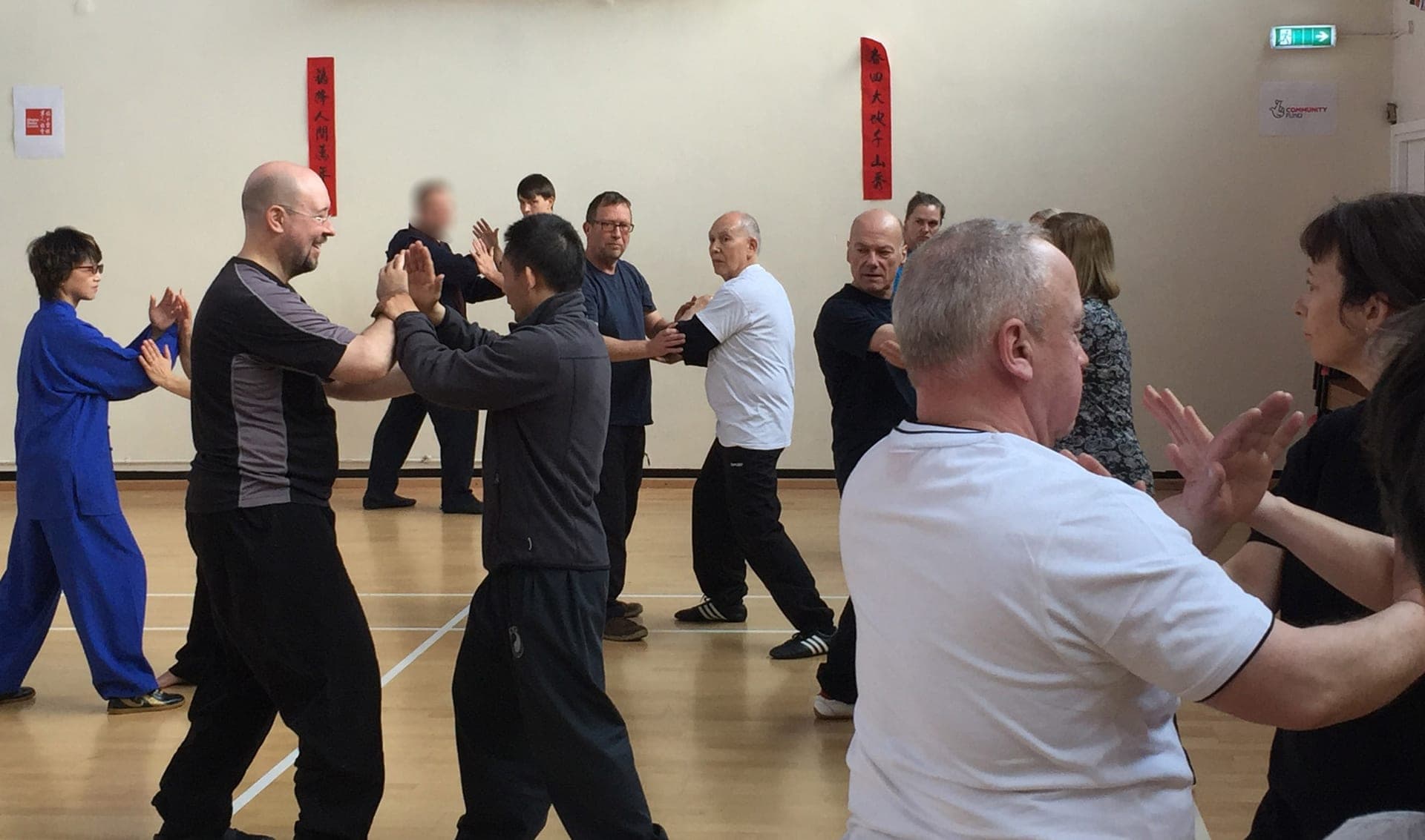 Pairs practising push hands across a sports hall