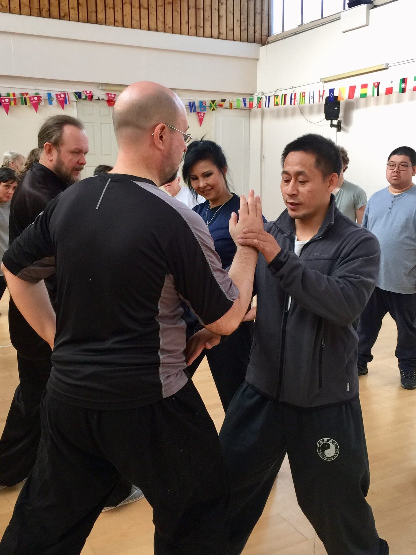 A teacher checks a student's posture during push hands, his hand on the student's arm
