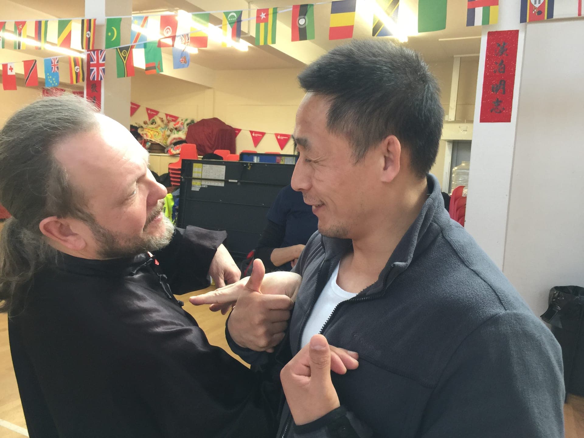 Close-up of a teacher demonstrating a Qinna lock on a bearded student's hand and arm