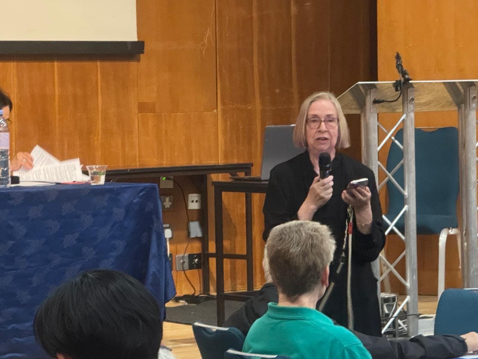 Chris Jones, in black with glasses, speaks into a microphone in front of a lectern at the Kensington & Chelsea Forum AGM, September 2026