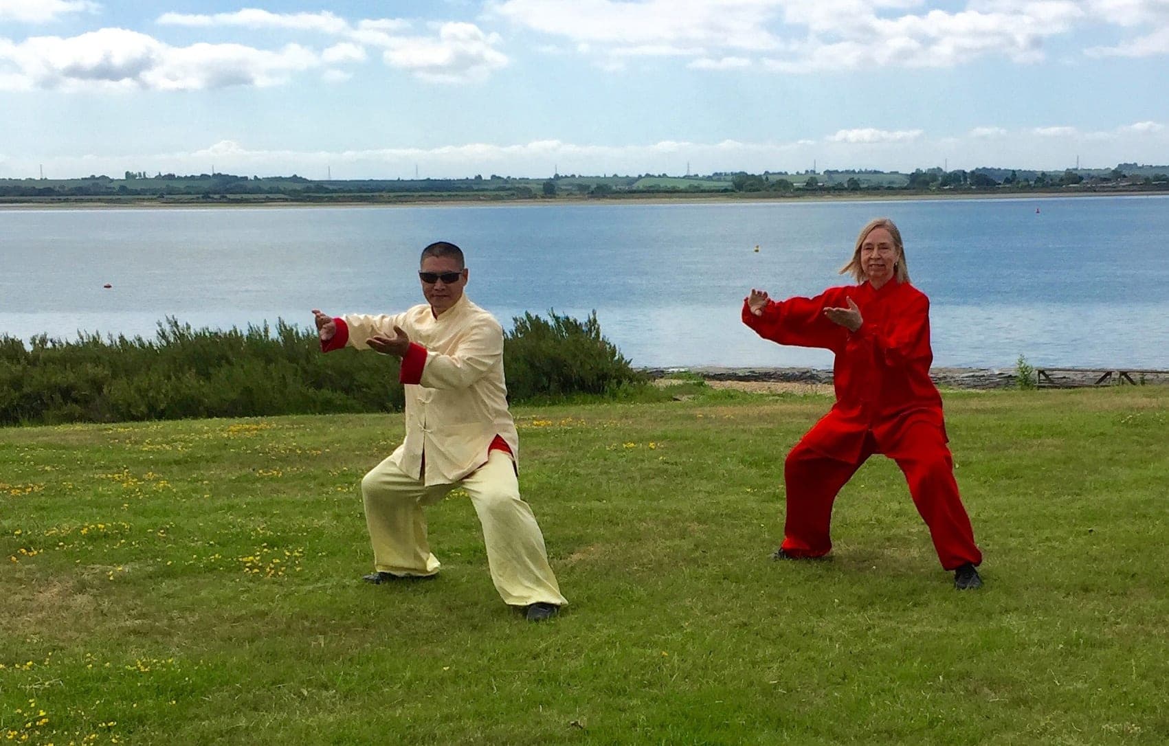 Chris Jones and Shifu Liu Quanjun holding the same Taiji posture side by side on a grassy bank above the water at Osea Island