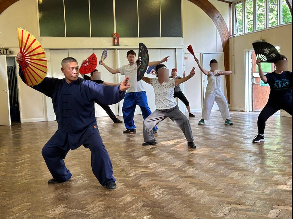 A teacher and students practising the Chen fan form with open fans in a hall