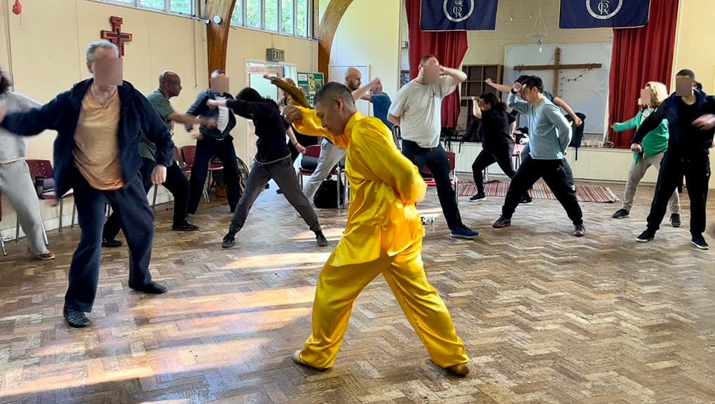 A teacher in yellow silk leading students through Jiu Jiu Gong in a hall