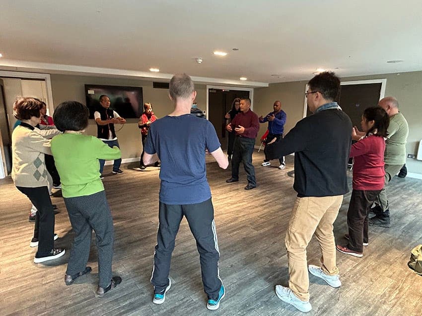 A circle of students in standing practice in a carpeted room during a free session