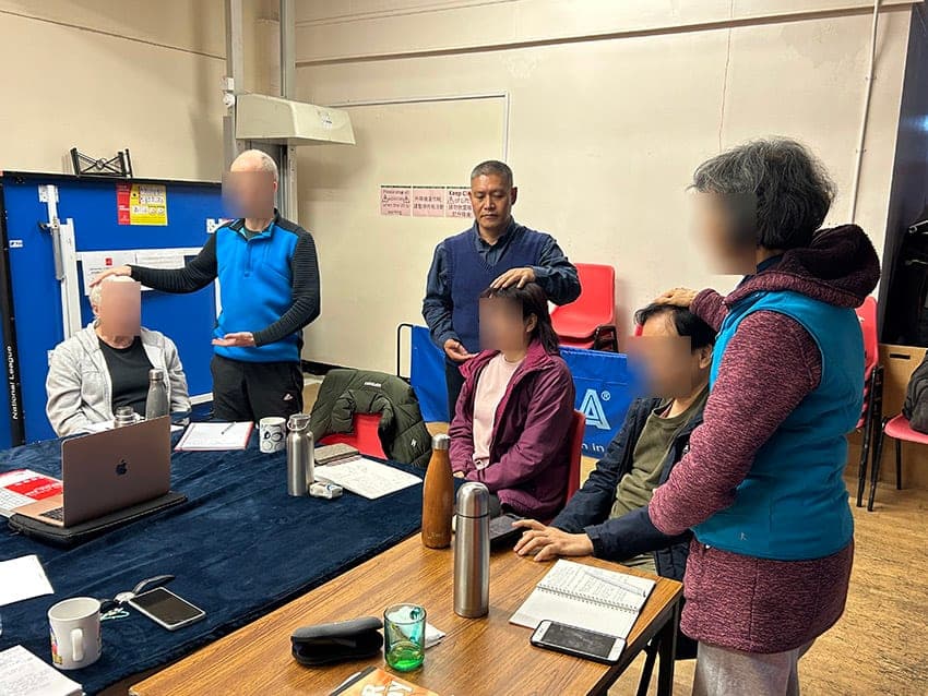 Shifu Liu showing students how to use qi healing, with their hands on seated partners' heads