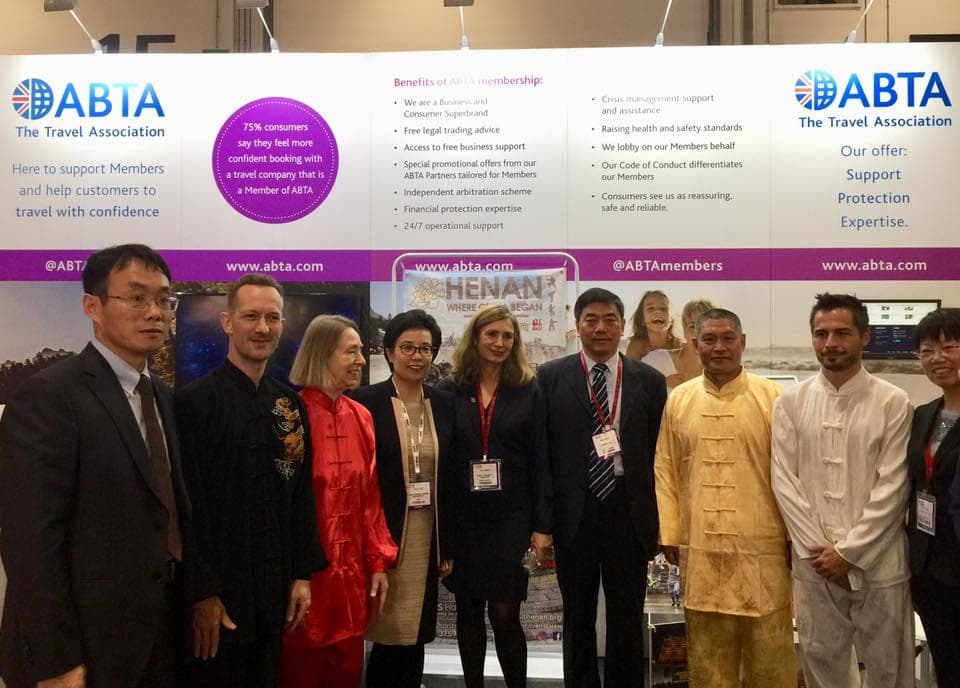 Tai Ji Circle members in silk uniforms standing with the Henan delegation in front of the ABTA stand at the ExCeL Centre