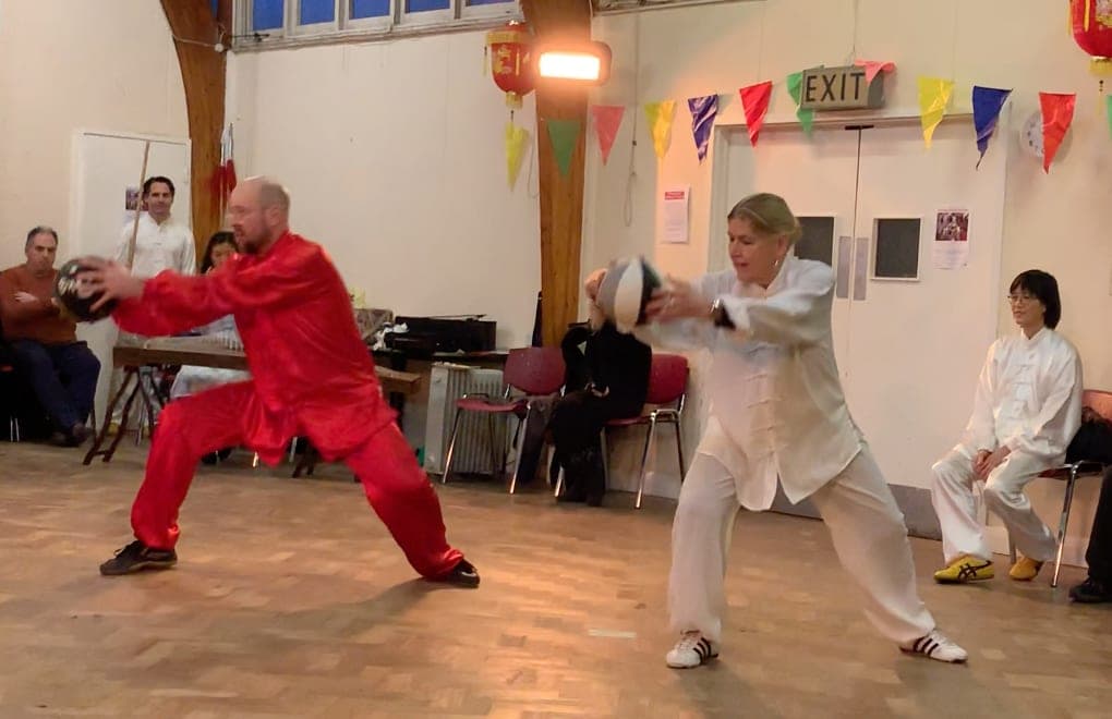 Two students, one in red and one in white, demonstrate Taiji ball training