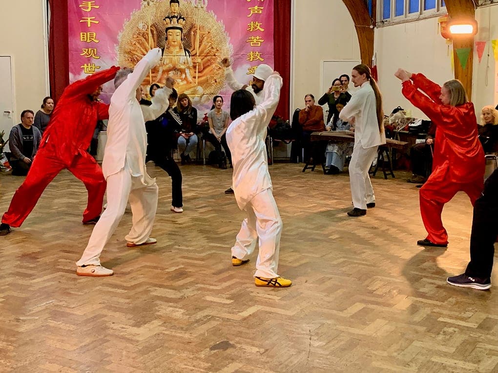 Students in red and white silk perform a Chen form in the round while guests and a guzheng player look on