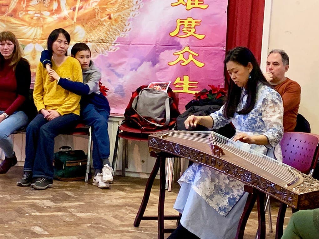 Joanna Zhenghui Qiu, in a blue and white dress, plays the guzheng while guests watch from chairs behind her