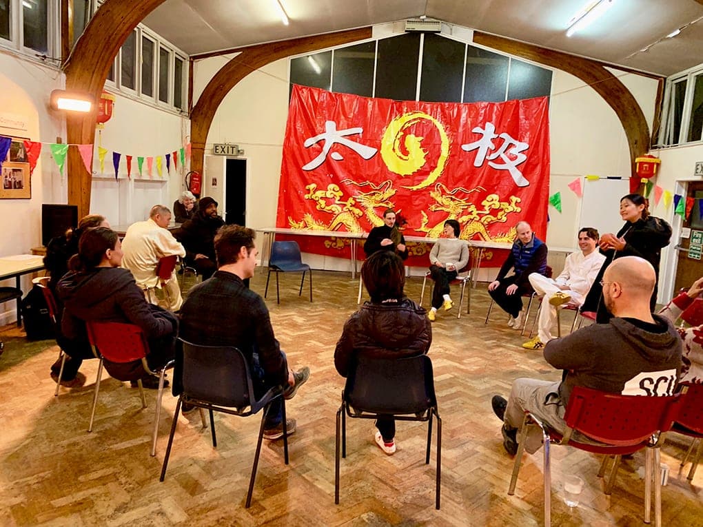 Guests sit in a circle of chairs for party games in front of the red Taiji banner