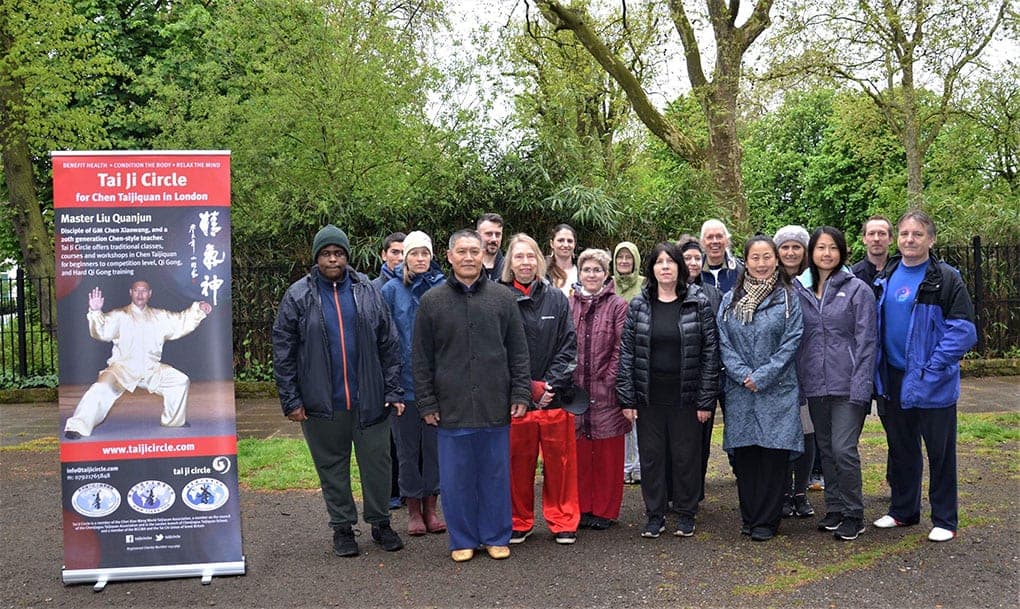 Shifu Liu with a group of students in winter coats beside a Tai Ji Circle banner in a tree-lined London square