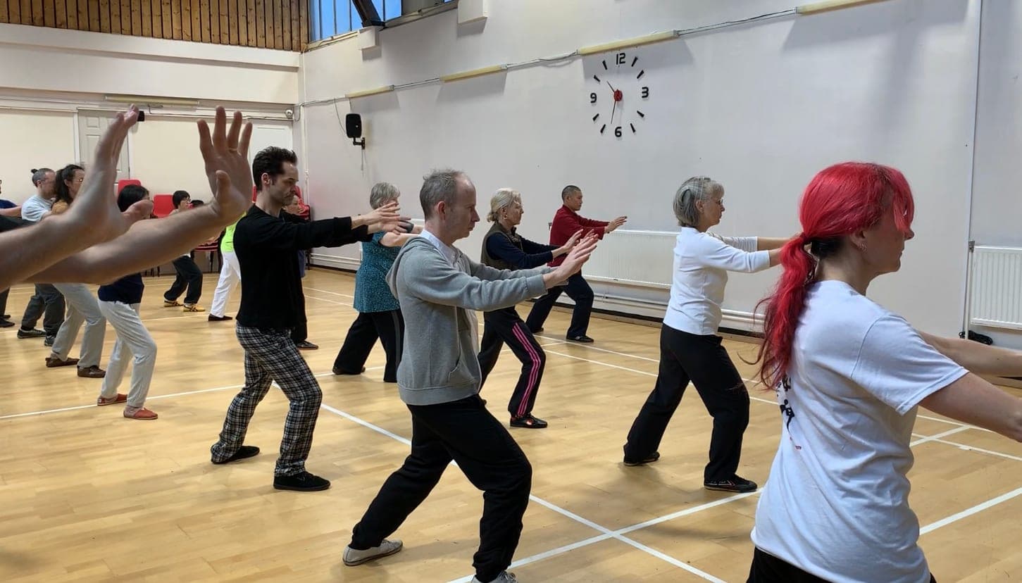Students in a sports hall practising a Yifei Gong movement, arms extended forward